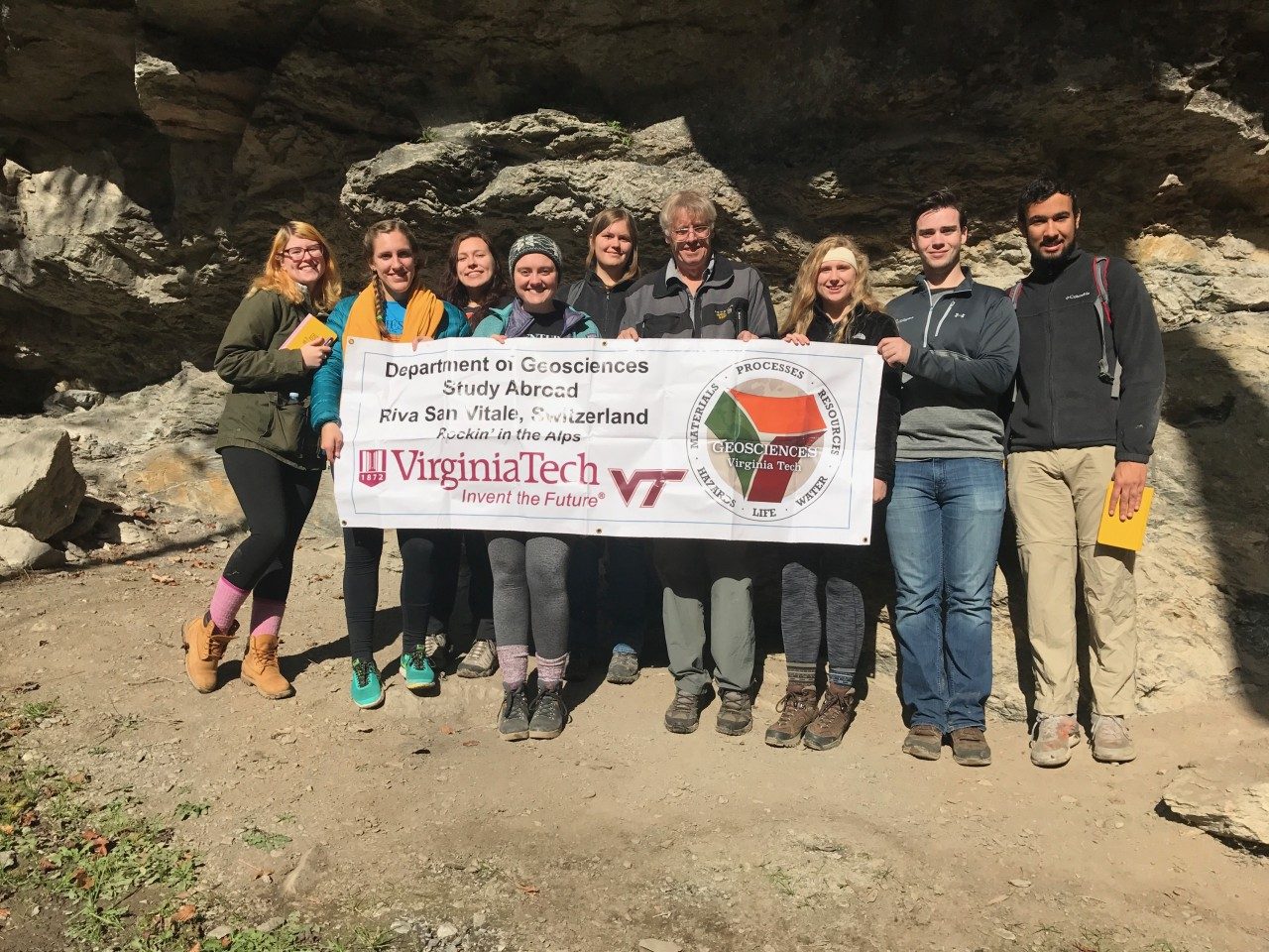 Photo of a group of 9 standing outdoors side-by-side holding a poster of the study abroad program in front of them