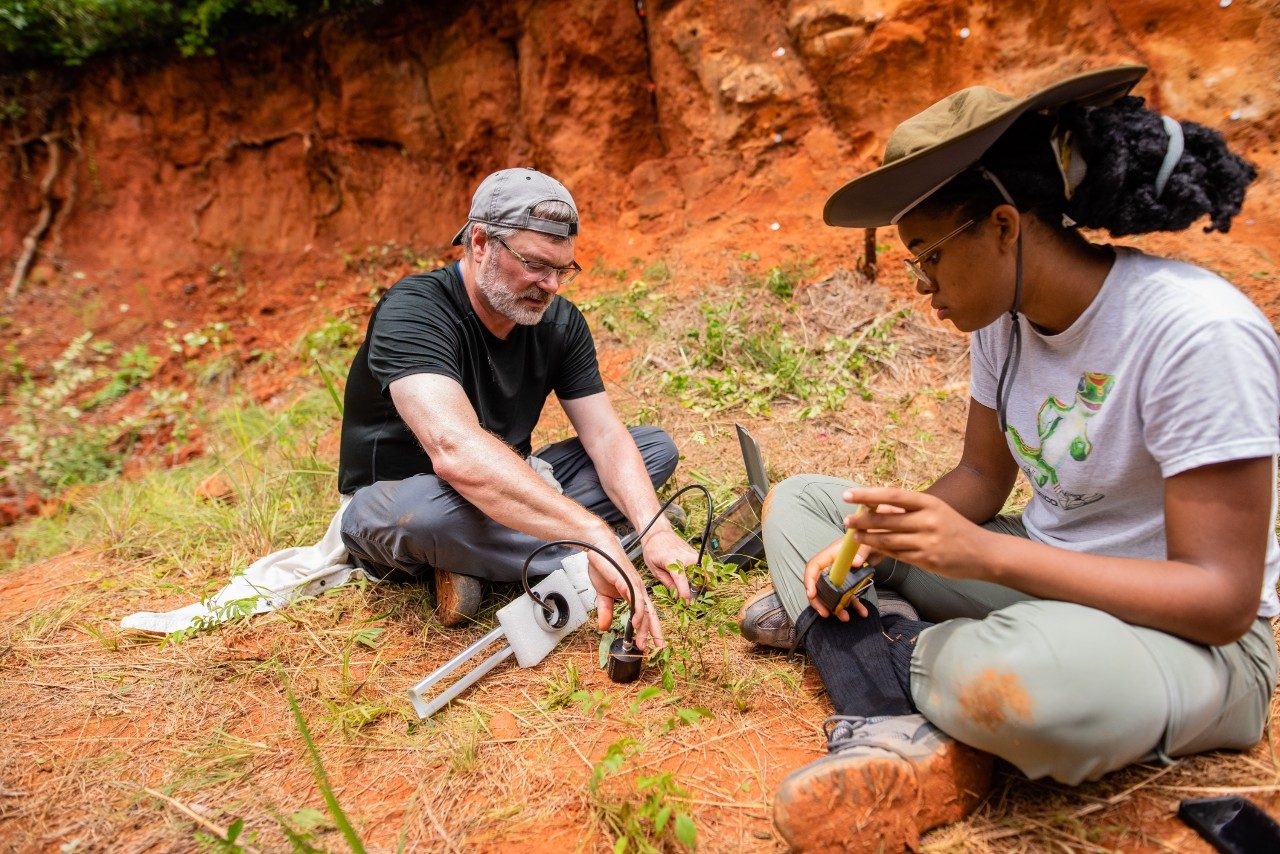 Two people sitting on the ground outdoors looking at field equipment