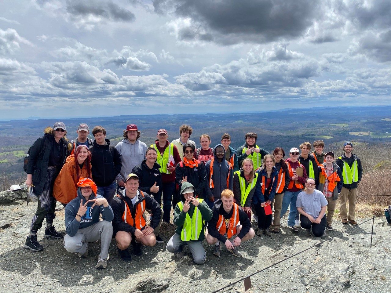 A group photo of 26 people outdoors standing in front of a landscape outlook