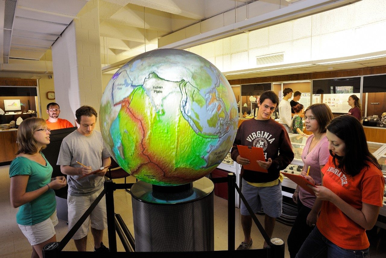 Five people surrounding a human-size globe in the Museum of Geosciences.