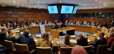 Scholars, government officials, and others sit around a large roundtable in a conference room at the United Nations headquarters.