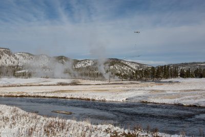 The SkyTEM instrument, attached to a helicopter, is photographed being flown over Old Faithful in Yellowstone National Park.  Photo by Jeff Hungerford, Yellowstone National Park; supplied by Carol Finn of U.S. Geological Survey.